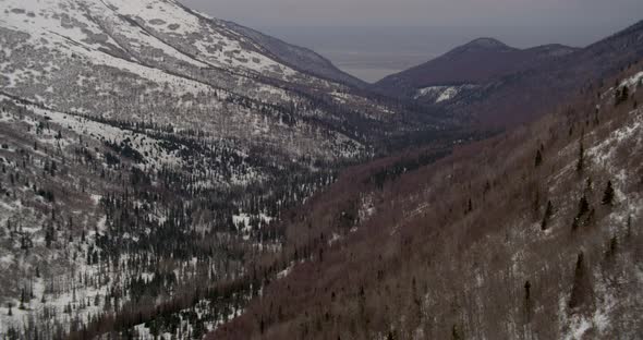 Aerial helicopter shot, circling around large snow-capped mountain surrounded by clouds on bright an