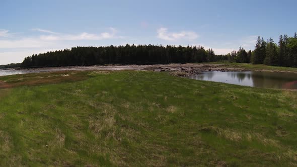 Smooth slow motion Drone footage of the Maine Coast flying over lush green coastal fields of grass w