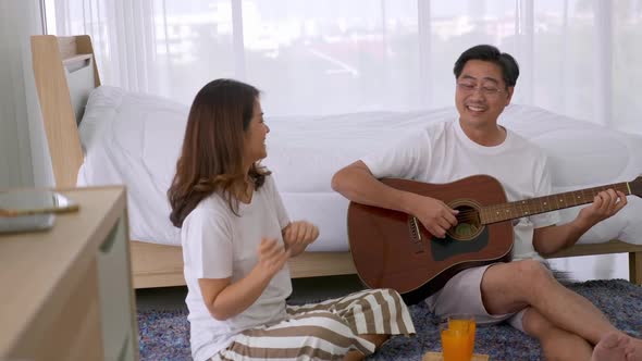 Happy Asian senior man playing guitar for his lover at the bedroom.