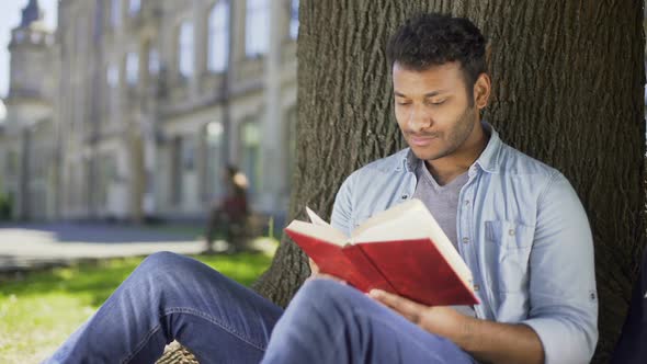 Male Reading Favorite Novel Under Tree Pressing Book Against Chest Daydreaming