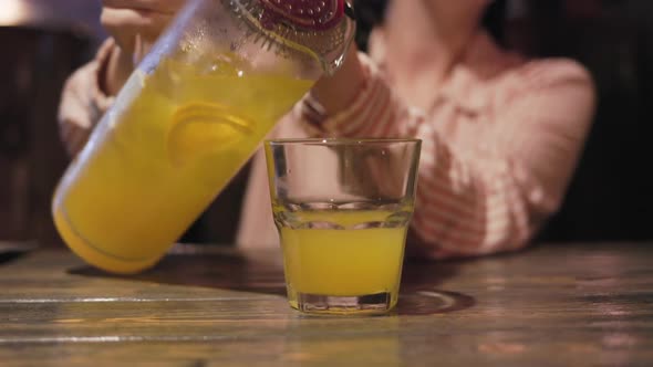 A woman pours a cocktail or orange juice from a decanter into a glass. Close-up