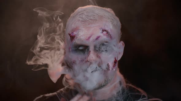 Sinister Man Halloween Zombie with Bloody Face Blows Smoke From Nose and Mouth Making Air Fly Kiss