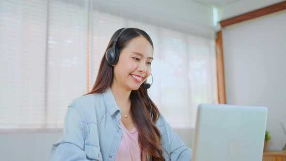 Asian Telemarketing or call center with headset talk and working on computer lap top at home office.