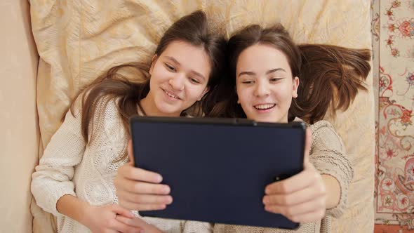 Happy Smiling Teenage Girls Relaxing on Bed and Having Online Video Conversation