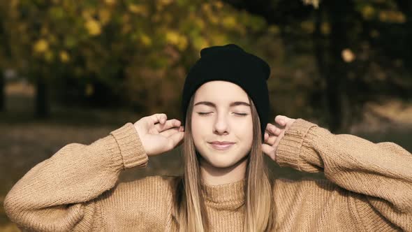 Pretty Girl in Hat Poses with Smile on Face at Camera in Sunny Autumn Park