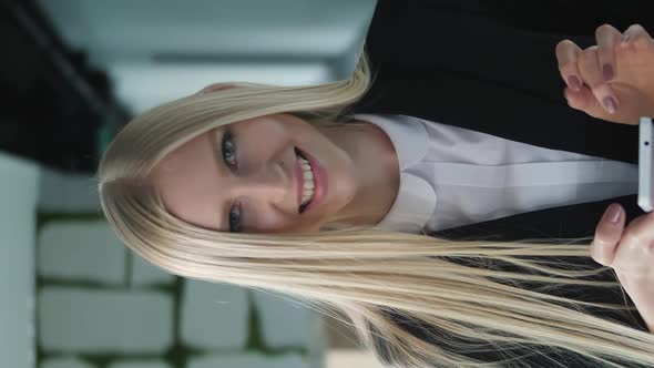 Cheerful Young Woman with Phone in Office. Pretty Blond Woman with Long Hair Wearing Elegant Black