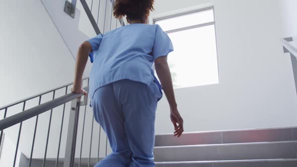 Mixed race female doctor wearing face mask running up the stairs in hospital