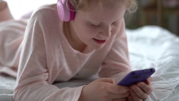 Modern Life of Generation Z. Teenage Girl in Pajamas and Headphones in the Room on the Bed Listens