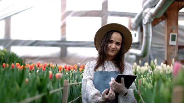 Portrait of a Beautiful Young Smiling Woman Gardener in an Apron Stands with a Tablet in a