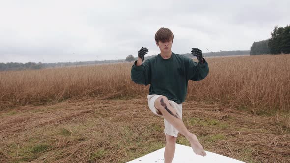 A Young Guy Performs an Alternative Dance in Nature and with His Hands Dipped in Black Paint Leaves