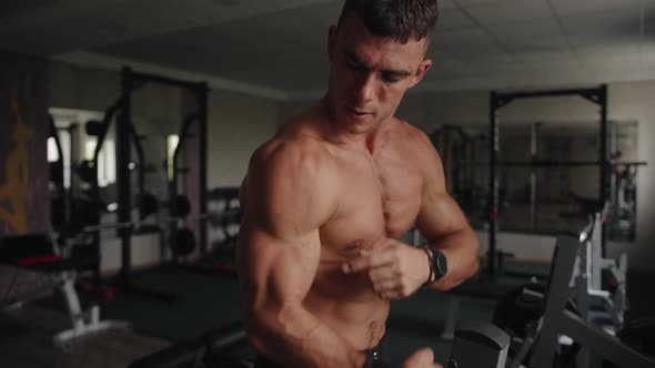 A Young Man with a Naked Torso Stands in the Gym After a Workout and Demonstrates the Pumped Up