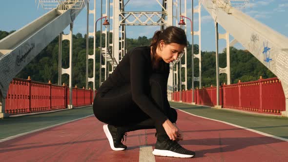 Attractive Woman Tying Shoelace on Sneakers on City Bridge and Starting To Run. Female Athlete Ties