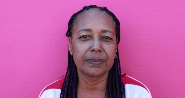 African senior woman looking serious on camera with pink background