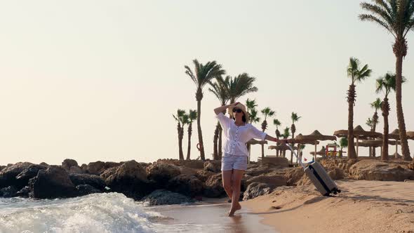 Young Woman in Summer Clothes and Sun Hat, Holding Travel Bag, Looking at the Sea, Enjoying the