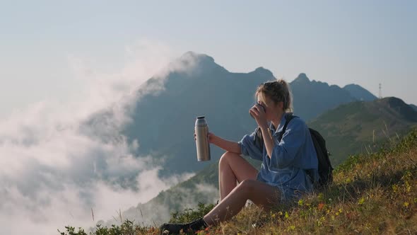 Happy Teenager Girl is Resting on Top of Mount and Drinking Tea From Thermos Bottle