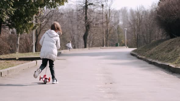 The Little Girl Is Driving a Scotter on a Park Alley