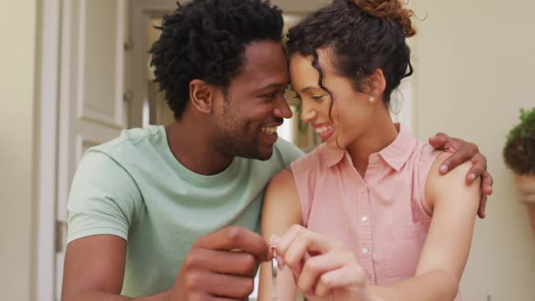 Happy biracial couple embracing with joy and holding keys in front of new house
