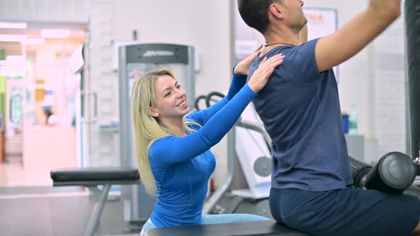 Young woman trainer monitors the correctness of the exercise by the man