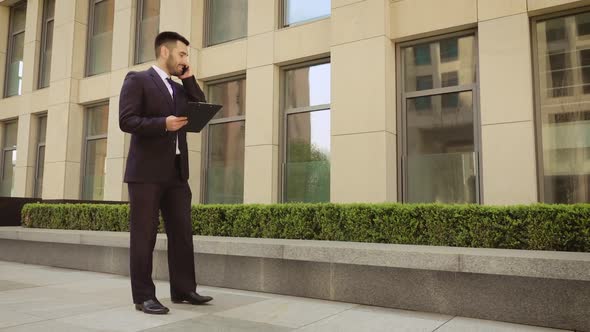 Very Angry Businessman Walks Down the Street with a Tablet and Talking on the Mobile Phone