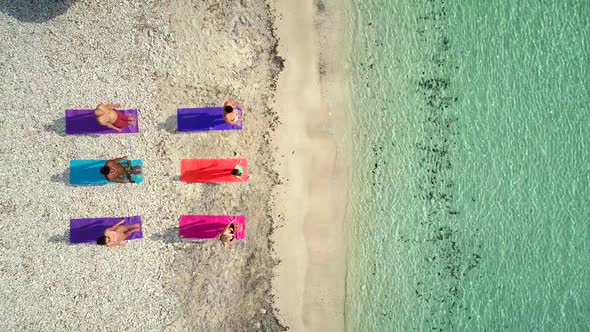 Aerial view of group of people doing yoga on colorful mats on sandy beach.