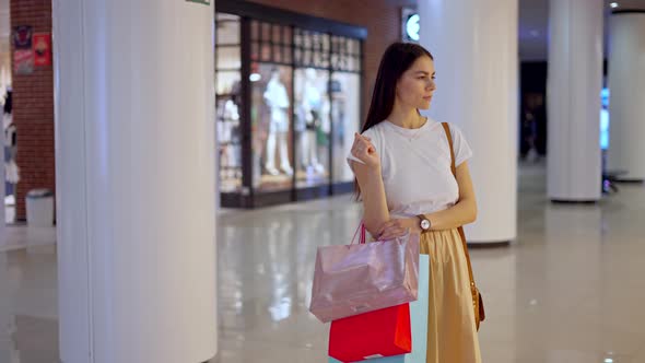 Female Shopaholic Standing in Front of Glass Showcase with New Clothing Collection at Shopping Mall