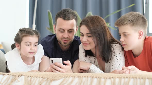 Happy American Family Relaxing on Sofa at Home They Use Smartphone and Have Fun Laughing