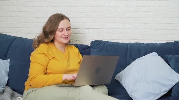 Woman is Sitting on the Sofa with Laptop and Typing Something