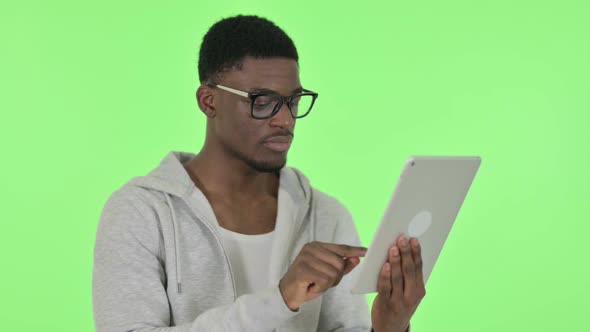 African Man Celebrating Success on Tablet on Green Background