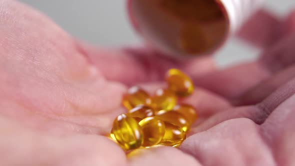 Falling soft gel omega 3 capsules into the palm with wrinkled dry skin from a white pill container