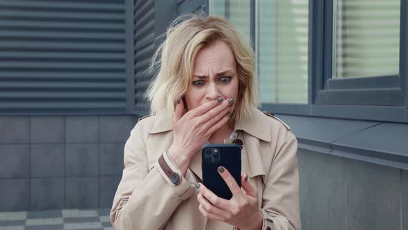 Upset Business Woman Looking with Horror at the Smartphone Screen and Covers Her Mouth with Her Hand