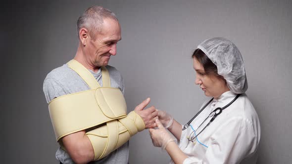 Lady Orthopedist Checks Hand Bones of Old Man with Bandage