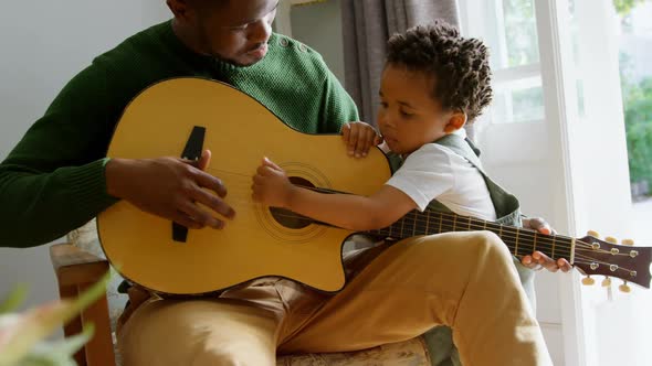 Front view of young black father and little son playing guitar in living room of comfortable home 4