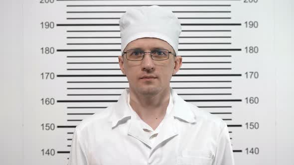 Mugshot of a Doctor in Glasses, in a White Coat, at the Police Station