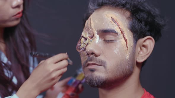 Make up artist coloring with make up brush Halloween mask on man's face