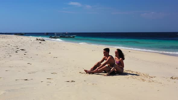 Cute couple with sunglasses sunbathe on white sandy beach at sunrise with blue sea background and wh