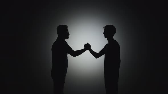 Black Silhouettes of Men Shake Hands in a Friendly Manner