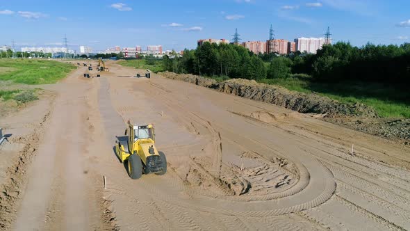 Yellow roller-compactor movies on sandy construction site in Moscow suburbs