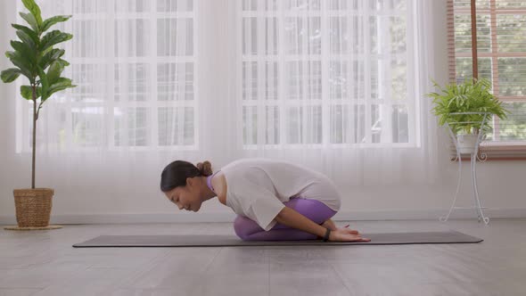 Asian woman working out in sportswear while doing yoga, seated in Child exercise, Balasana stance.