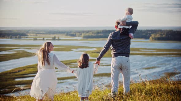 Young Family Standing on the Field and Holding Hands While Looking at River