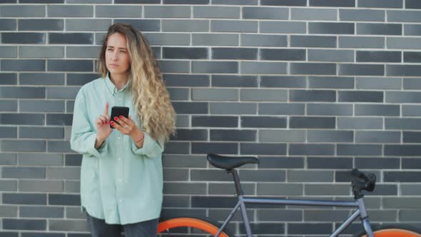 Woman Standing with Bike on Street and Using Smartphone