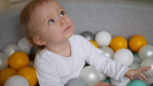 Girl in a White Bodysuit Plays with Colorful Plastic Balls in Dry Pool