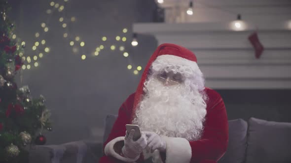 Santa Claus Sitting on Couch and Talking on Smartphone