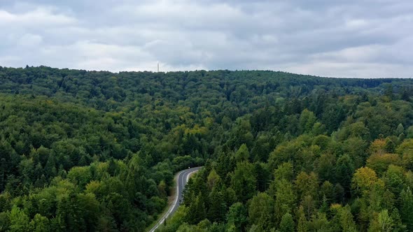 Car moves on a winding road among forest and mountains. Aerial drone view, zoom in