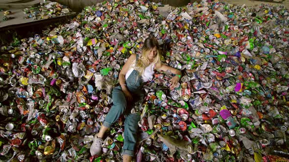 High Angle Young Woman Lying in Huge Pile of Trash and Looking at you