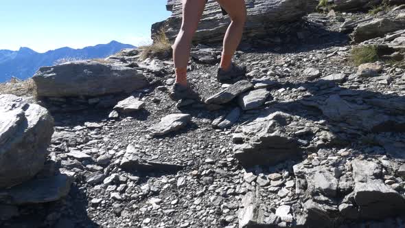 One person hiking on the mountains, close up body parts feet legs, dramatic rocky terrain, rear view