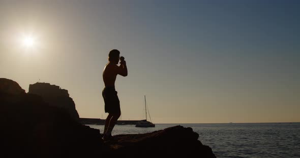 Silhouette of a boy does boxing on the rocks by the sea