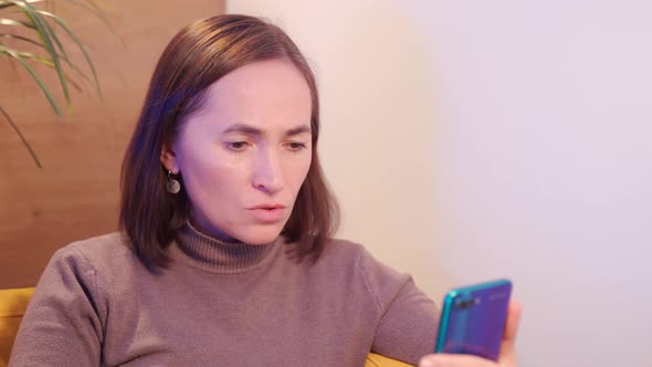 Happy Woman Sits in a Chair and Chats on Social Networks Using Mobile Phone Smartphone