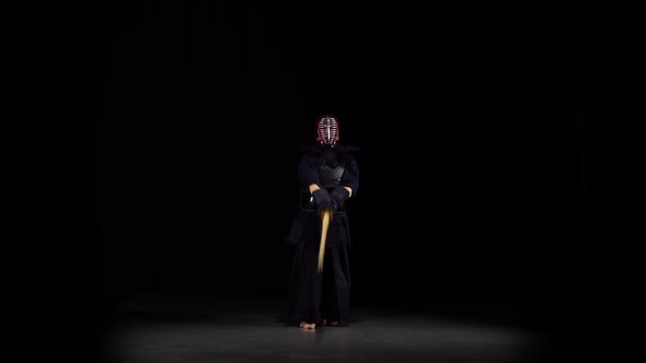 Strong Kendo Guru Practicing Martial Art with the Bamboo Bokken on Black Background.