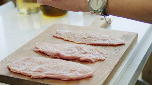 Woman adding pepper to raw veal schnitzel on board