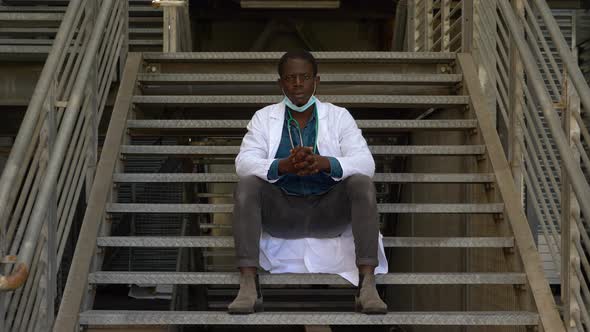 worries, thoughts - black doctor with the mask pulled down stares at camera